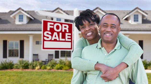 Happy African American Couple In Front of Beautiful House and For Sale Real Estate Sign.