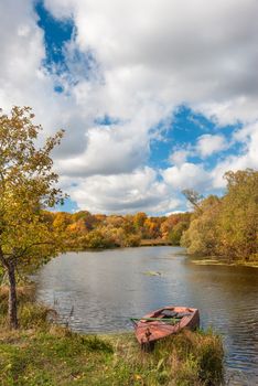 Beautiful autumn landscape with old boat on the riverbank against a forest