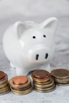 Concept of investing or saving: white ceramic piggy bank and a few piles of euro coins