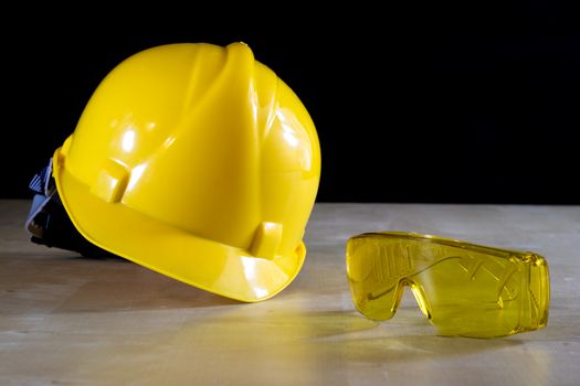 Yellow helmet, safety goggles and work gloves for the worker, black background