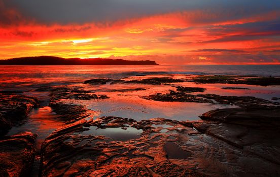 Rich red velvet sunrise casts its hues over Pearl Beach, the ocean and the rocks and rock pools in the foreground