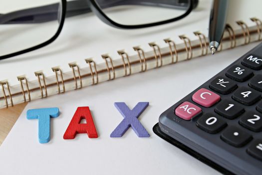 Business, finance, saving money, investment, taxes or accounting concept : Wooden word TAX, notebook paper and calculator on office desk table