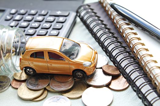 Business, finance, saving money, banking or car loan concept : Miniature car model, calculator, coins scattered from glass jar, notebook paper and pen on office desk table