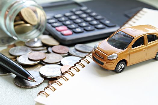 Business, finance, saving money, banking or car loan concept : Miniature car model, calculator, coins scattered from glass jar, notebook paper and pen on office desk table