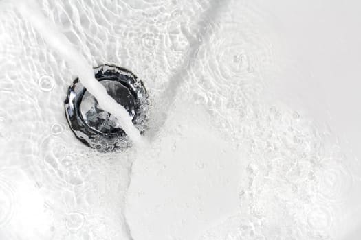 Fresh water running down the drain of a ceramic washbasin