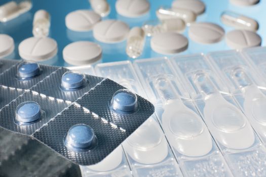 Blue pills in strip with ampoules, white pills and capsules with medicine in blue background