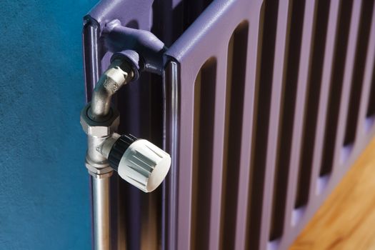 Thermostat on a purple central heating radiator and a blue wall 