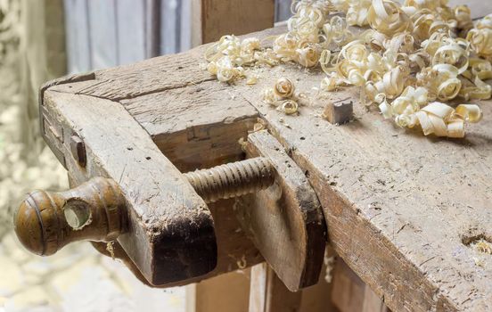 Fragment of old woodworking workbench with two fixing device of workpieces - planing stop and shoulder vise with wooden screw and shavings on workbench
