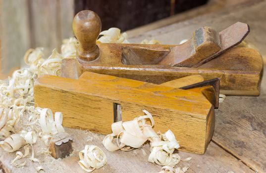 Two old wooden hand planes different purposes among a shavings on the old woodworking workbench with planing stop on foreground
