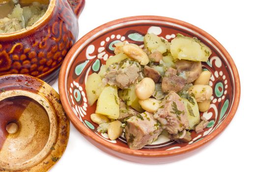 Ukrainian version of the dish Chanakhi - potatoes with meat, mushrooms and haricot beans roasted in a clay pot in a clay bowl on a white background closeup 
