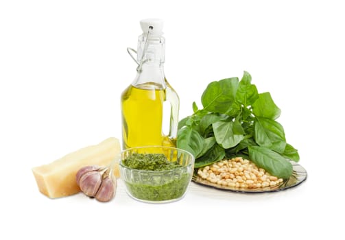 Sauce basil pesto in the small glass bowl and ingredients for its preparation on a white background
