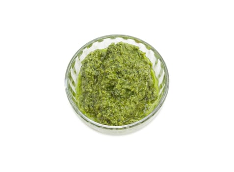 Top view of the sauce basil pesto in the small glass bowl on a white background
