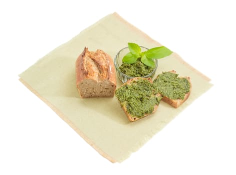 Two sandwiches with sauce pesto, part of bread and sauce basil pesto in small glass bowl decorated with green basil twig on a napkin on a white background
