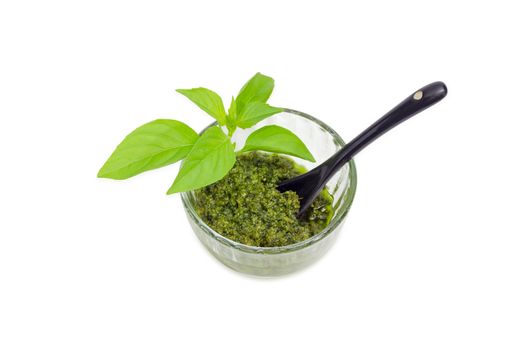 Sauce pesto in the small glass bowl with small black ceramic spoon and decorated with green basil twig on a white background
