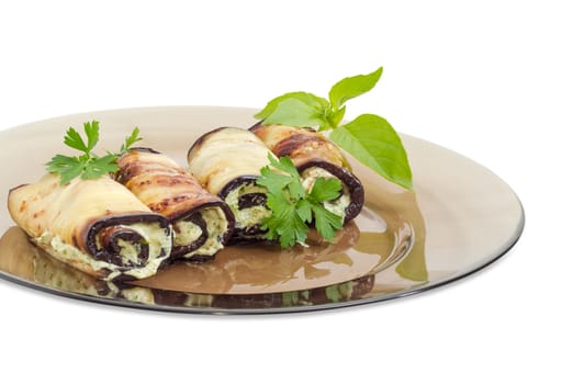 Fragment of a dark glass dish with several eggplant rolls stuffed with tuna and processed cheese and decorated with parsley and basil twigs on a white background  closeup
