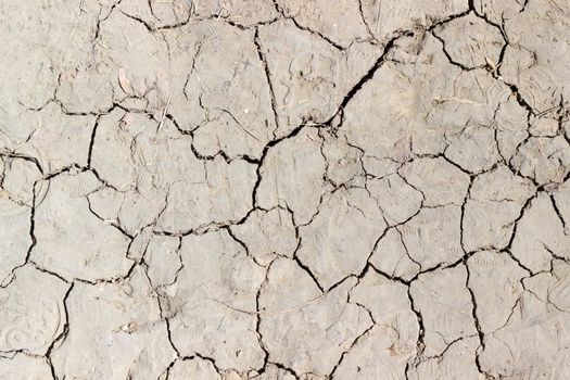 Texture of a fragment of the dirt track with cracks in dried ground and footprints of shoes during drought closeup
