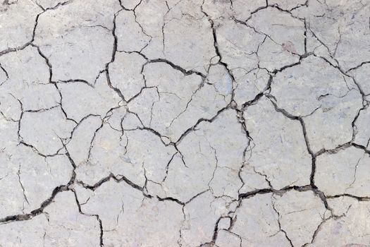 Texture of a fragment of the dirt track with cracks in dried ground during drought closeup
