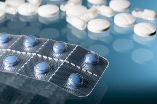 Blue pills in strip with white medicine pills and capsules in blue background