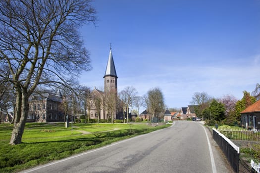 Asphalted road in village Kethel with church Jacobuskerk in the Netherlands