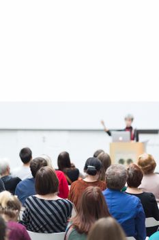 Business and entrepreneurship symposium. Female speaker giving a talk at business meeting. Audience in conference hall. Rear view of unrecognized participant in audience. Copy space on whitescreen.