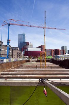 Construction site with 2 cranes in Rotterdam, in the Netherlands. Modern architecture and old warehouses in the background.