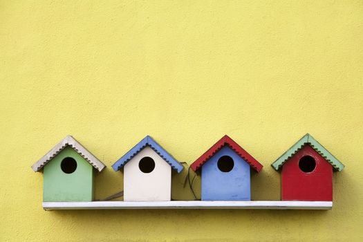 Street of four colorful birdhouses hanging on a yellow wall