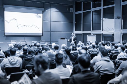 Speaker giving a talk in conference hall at business event. Audience at the conference hall. Business and Entrepreneurship concept. Black and white blue toned image.