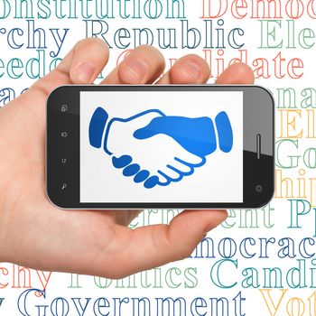 Politics concept: Hand Holding Smartphone with  blue Handshake icon on display,  Tag Cloud background, 3D rendering