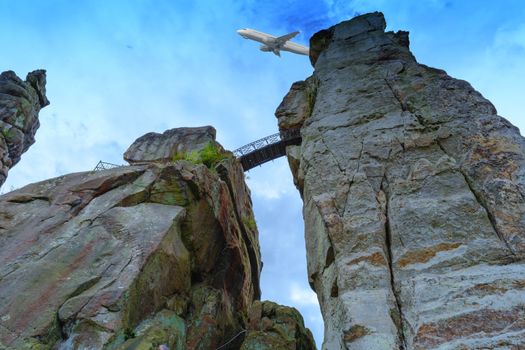 The external stones, marked sandstone rock formation in the Teutoburg Forest, Germany, North Rhine Westphalia. In the background in the sky a commercial aircraft.