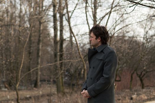 Portrait of a young handsome man sad looking to the left in the park, the woods in autumn or spring. Portrait on the nature of the park, the woods, on the street, horizontal picture. Real people series