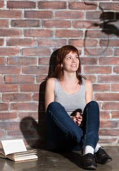 Caucasian girl sitting on the floor reading a horror or scary thriller book. Dramatic lighting with girls eyes wide open and long shadows of hands with noose on the wall near her. Terrified expression.