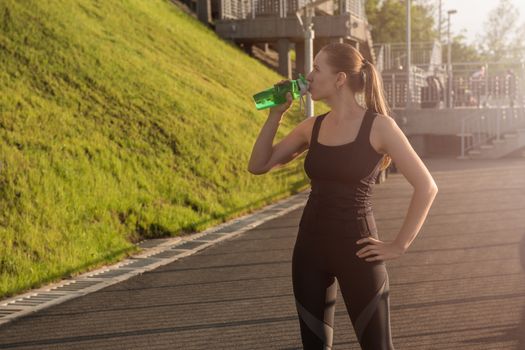 A woman in sportswear with bottle of water have rest at sunset on the evening city background