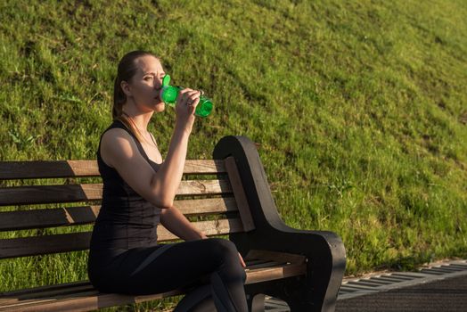 A woman in sportswear with bottle of water have rest at sunset on the evening city background
