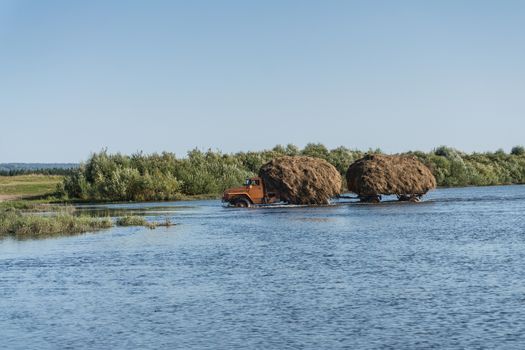 A truck with a trailer carries hay through the river