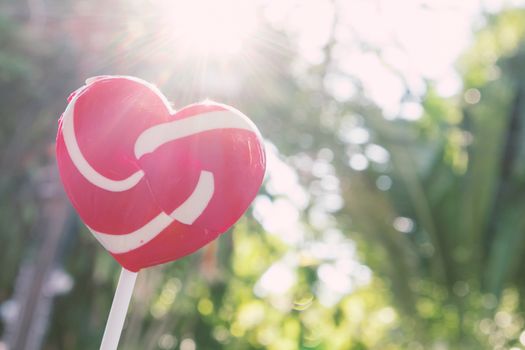 Sweet red heart lollipop with light of sun and nature background, love concept