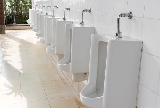 Closeup urinals white color in men's public restroom with light of sun