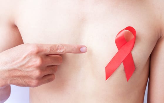 Hand pointer finger to red ribbon on chest for AIDs awareness concept