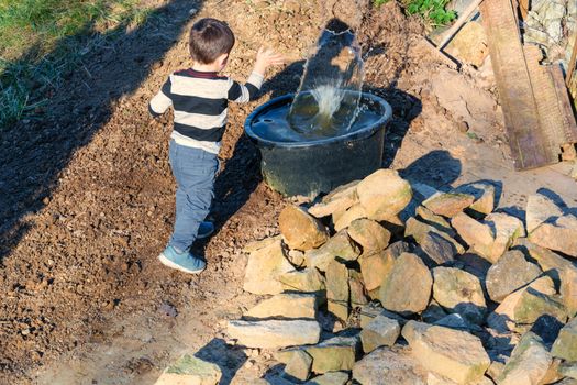 Little boy throwing a stone into a water barrel