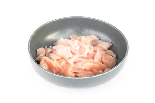 Pieces of raw chicken fillet in bowl on white background, raw material for cooking