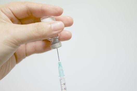 Hand of nurse holding hypodermic syringe suck vaccine from vial with white background.