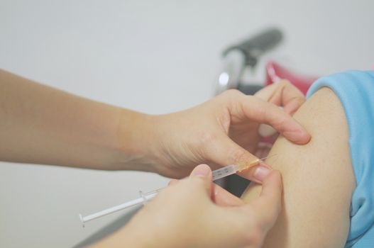 Hand of nurse holding hypodermic syringe to inject vaccine with patient on wheelchair with white background.