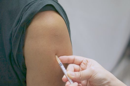 Hand of nurse holding hypodermic syringe has injected vaccine with patient man in black T-shirt.