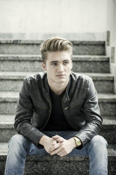 Attractive blond young man, sitting on stairs outdoors looking to a side