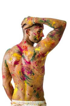 Handsome young man seen from the back with skin all painted with Holi colors, isolated on white background