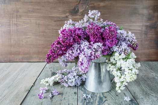 Lush wet multicolored bouquet of lilac flowers in a metal pitcher on an old wooden background