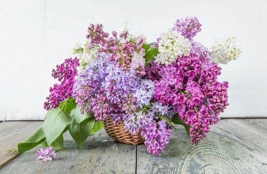Lush multicolored bouquet of lilac flowers in a basket on an old wooden background