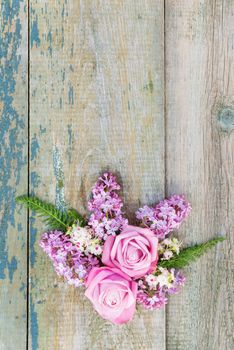 Decorative composition consisting of pink roses, violet lilac flowers and green leaves on the old wooden background. Flat lay, top view, with copy-spase