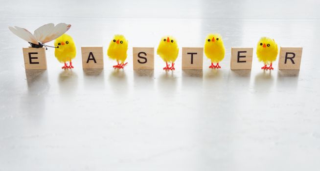 Easter concept: inscription Easter, consisting of wooden game pieces with letters, and yellow furry small fun chickens on a stone background