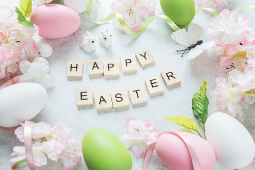 Beautiful delicate Easter composition with pink cherry flowers, multicolored Easter eggs, Easter bunny, butterfly and inscription "Happy Easter" on the stone background