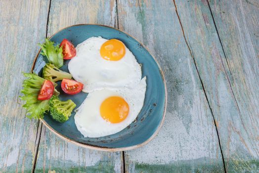 Breakfast consists of fried eggs and vegetables on the old wooden table, rustic style